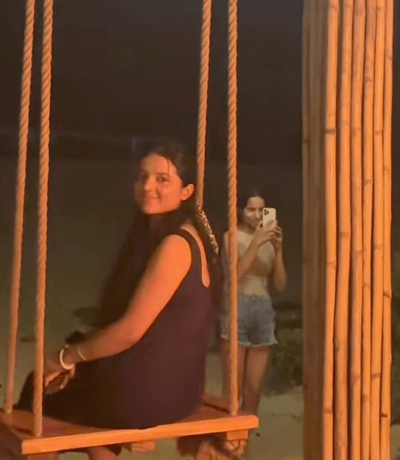 Shivangi on a wooden rope swing at night in a dark dress, glancing back with a soft smile