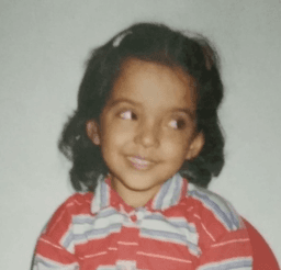 Shivangi as a young child in a striped polo with a gentle sideways smile