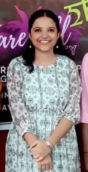 Shivangi at a farewell event in a white patterned midi dress, smiling with hands gently clasped