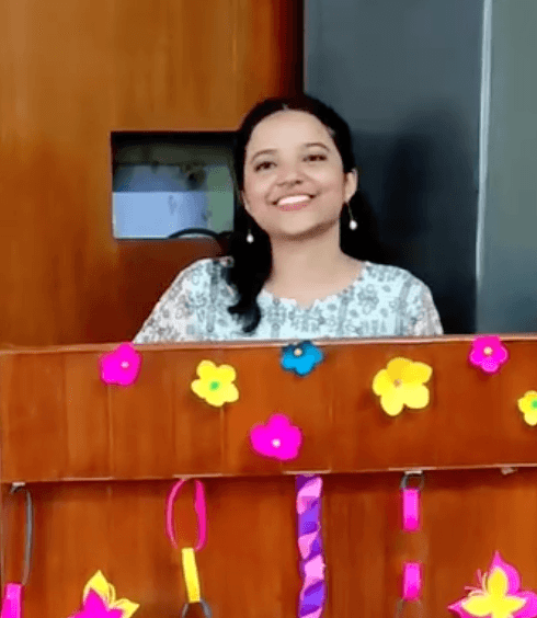 Shivangi smiling behind a desk decorated with DIY paper flowers, chains, and butterflies