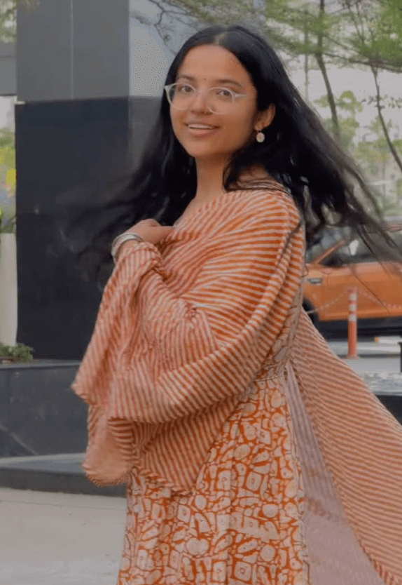 Shivangi outdoors in an orange and white block-print kurta with a striped dupatta, hair caught in the breeze